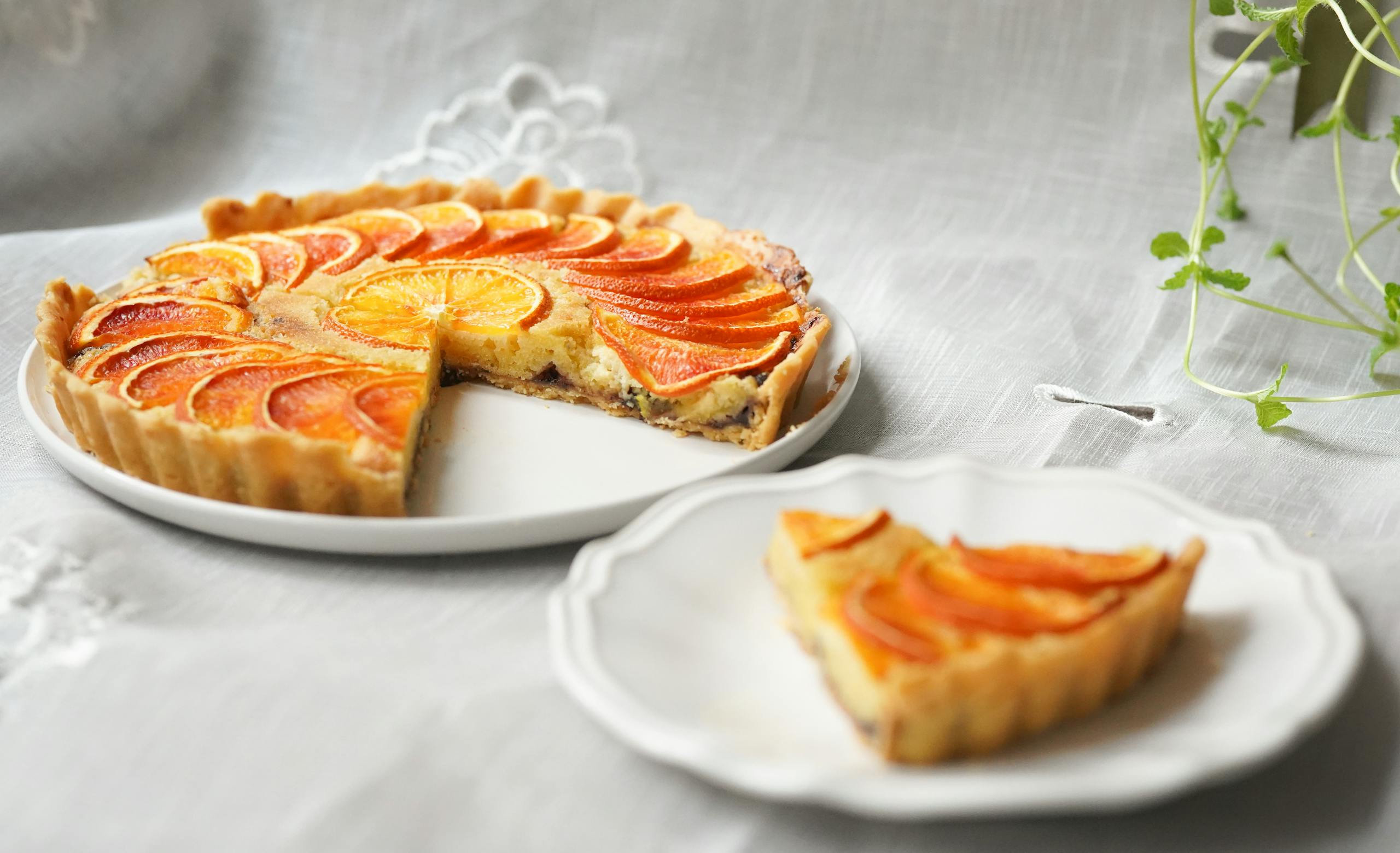 A sliced orange tart on a white plate set on a linen tablecloth, highlighting its vibrant citrus design.